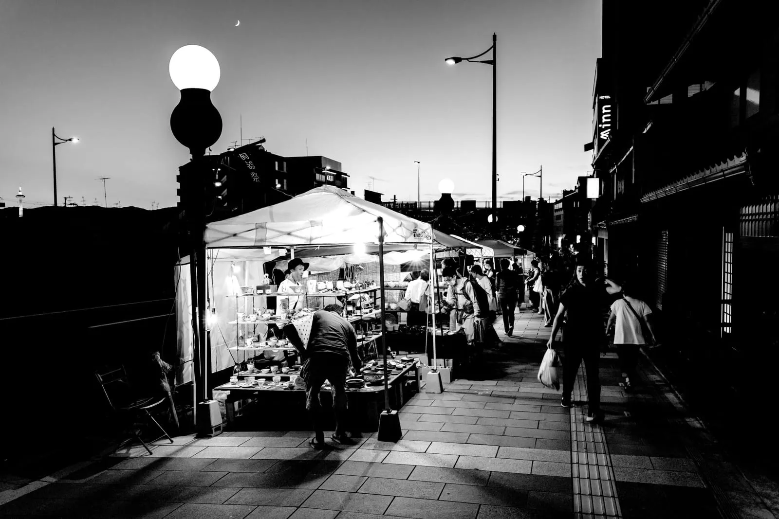 夜の五条若宮陶器祭。露店のテントと球形の街灯が並ぶ石畳の通りを行き交う人々